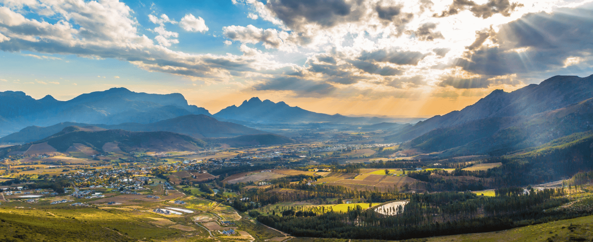 Los viñedos de Franschhoek con nubes y rayos de sol sobre ellos.