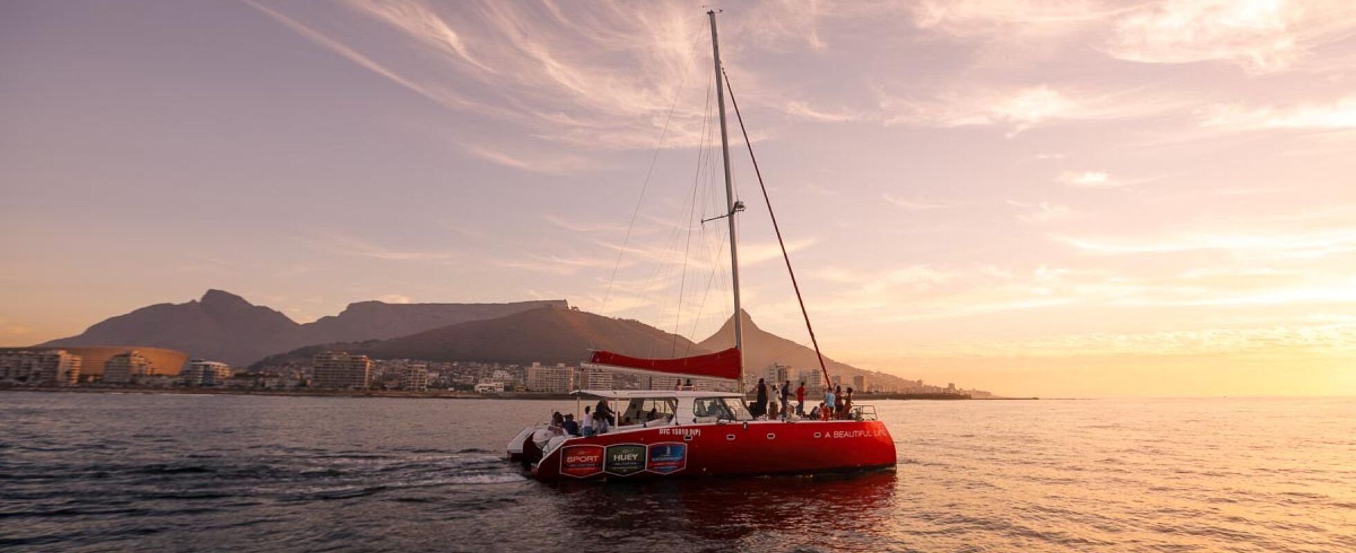 Velero frente a una costa montañosa con la puesta de sol