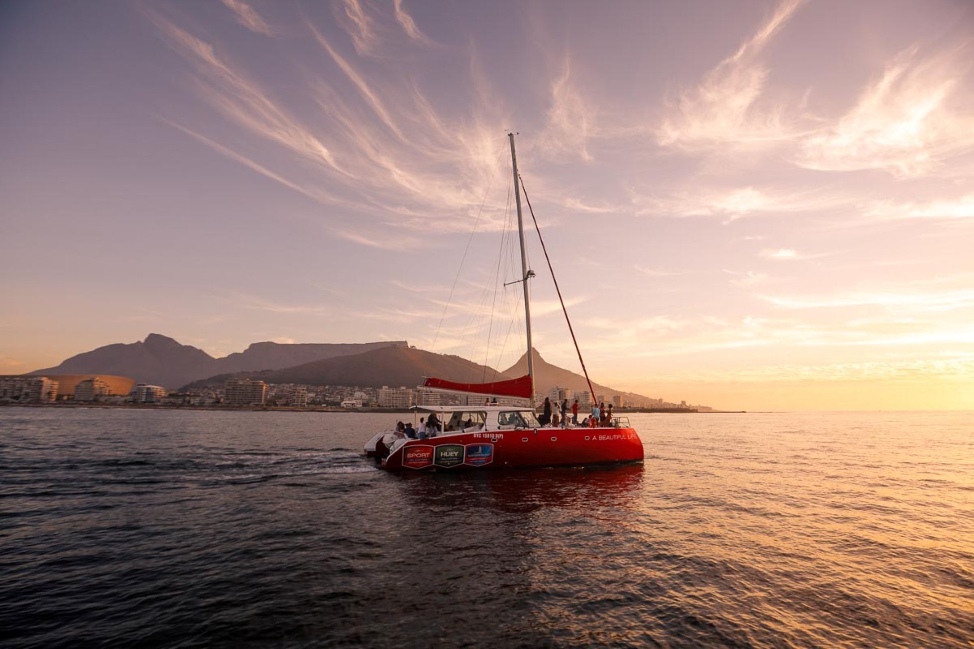 Velero frente a una costa montañosa con la puesta de sol