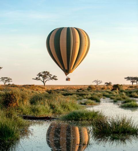 Globo aerostático sobrevolando el Serengueti y reflejado sobre el agua